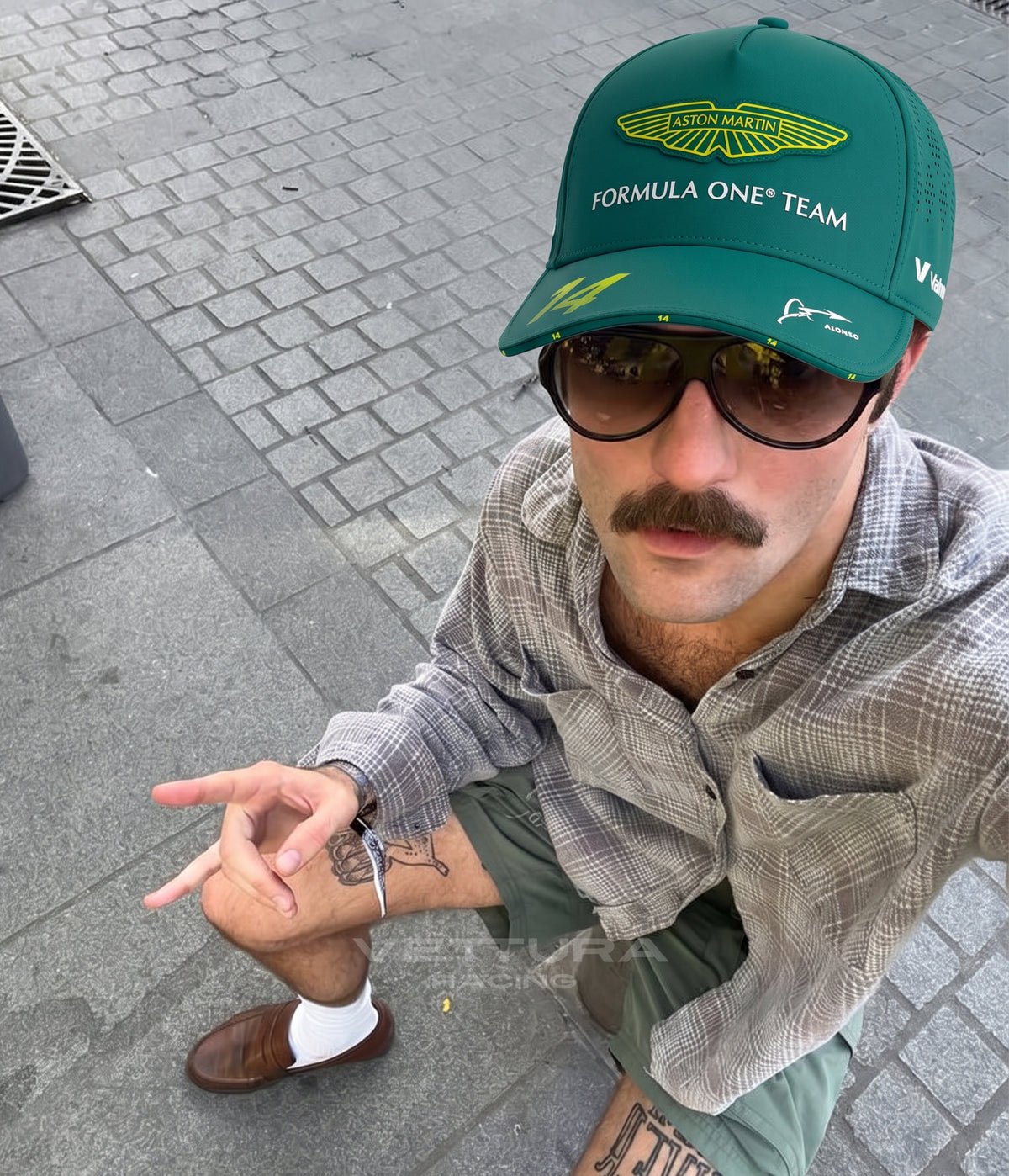 Man in sunglasses wearing the racing green Aston Martin F1 Alonso cap on a paved street