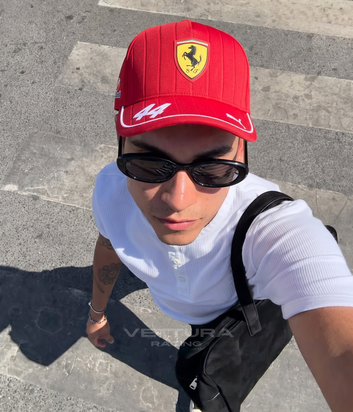 Man in sunglasses wearing the red Ferrari F1 cap with number 44 on a sunlit street