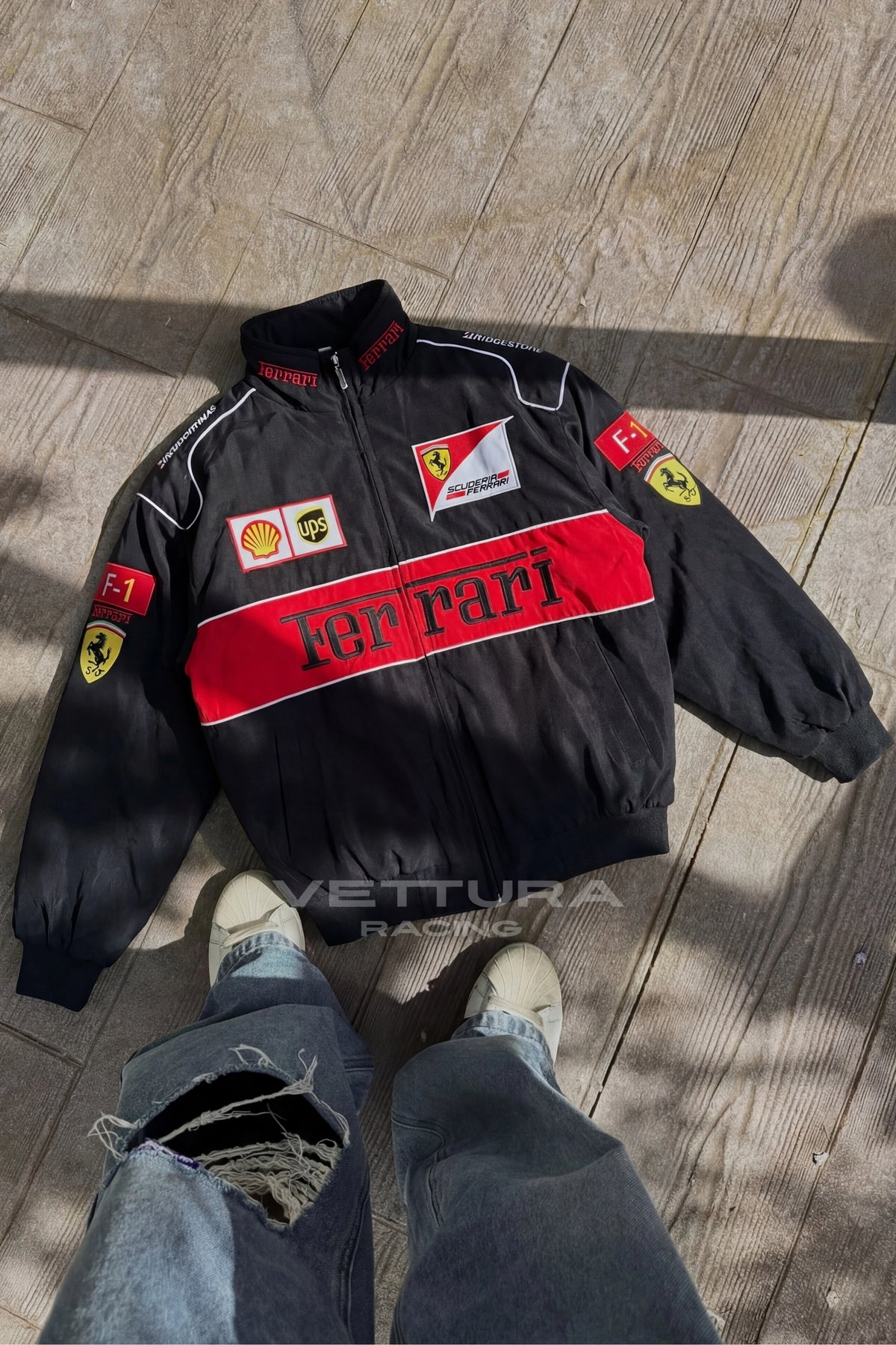 Detail of the black Ferrari F1 racing jacket laid flat, embroidered sponsor patches in close-up