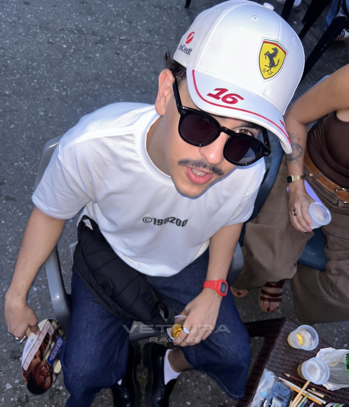 Man wearing the white Ferrari F1 cap with number 16, seen from above on a street
