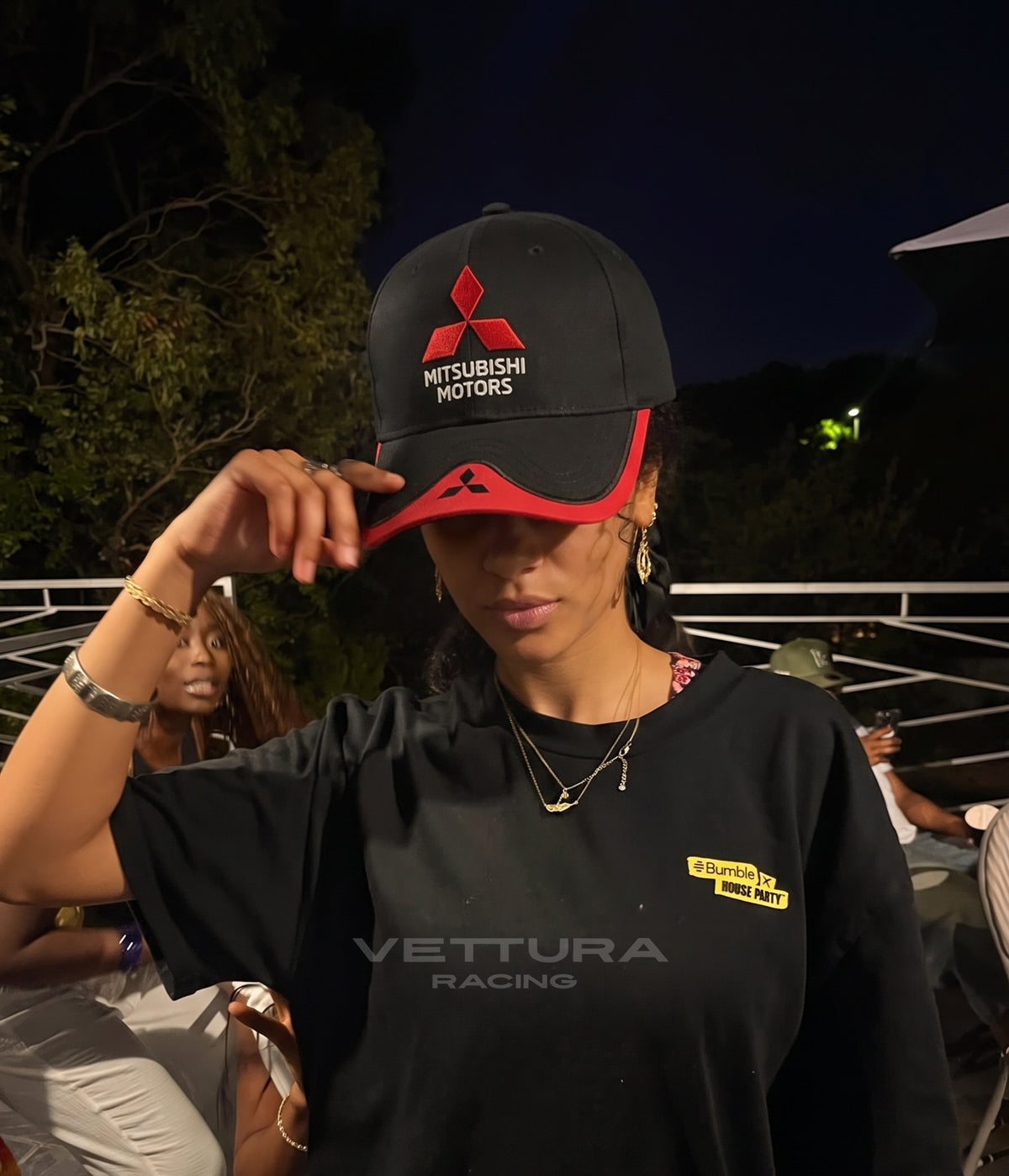 Woman wearing the black and red Mitsubishi Motors cap at an outdoor evening event