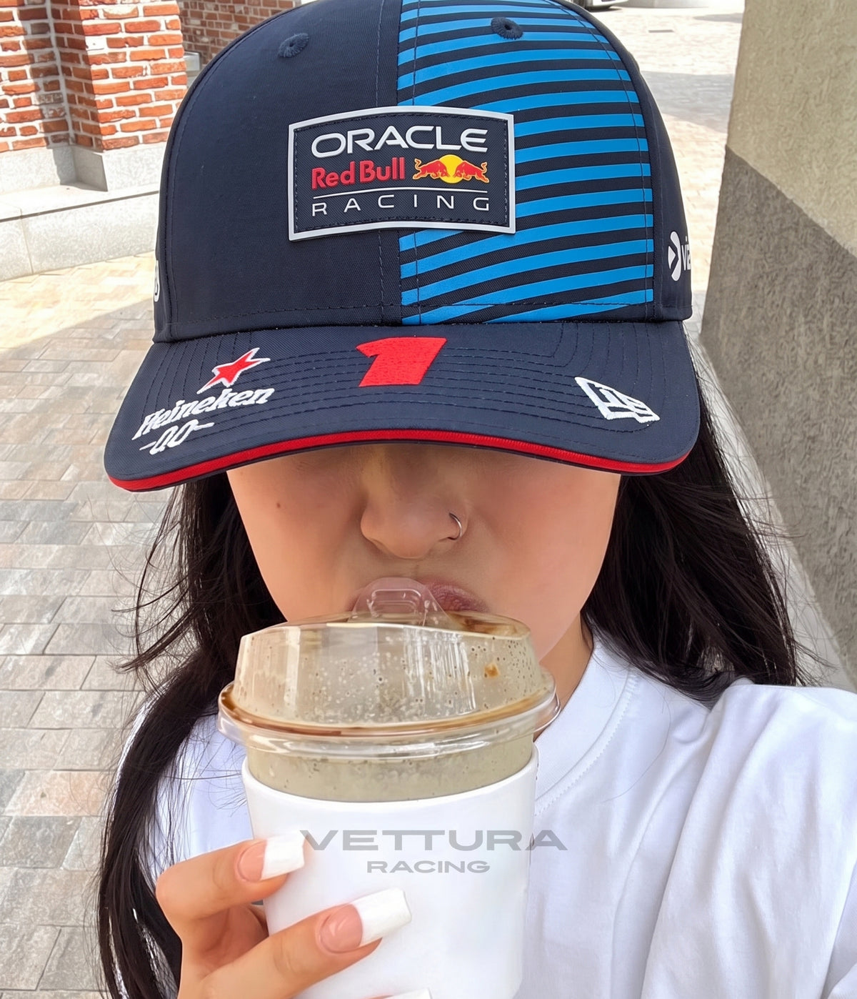Woman wearing the navy Red Bull Racing 2024 striped cap while holding an iced coffee