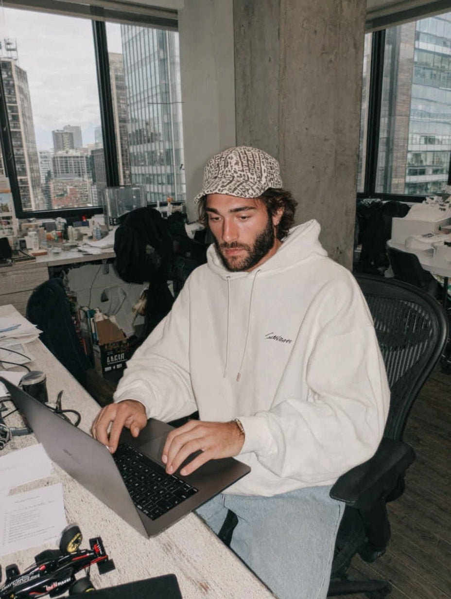 Vettura Racing designer in a white hoodie working at a laptop, vintage racing jackets on the studio rails