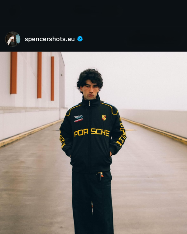 Man in a black Porsche vintage racing jacket standing on an empty road
