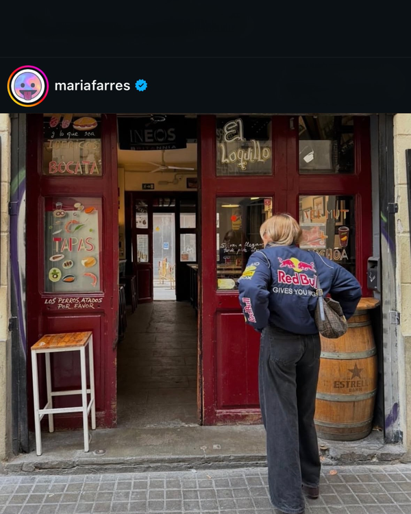 Back view of a woman in a navy Red Bull F1 vintage racing jacket at a shop entrance