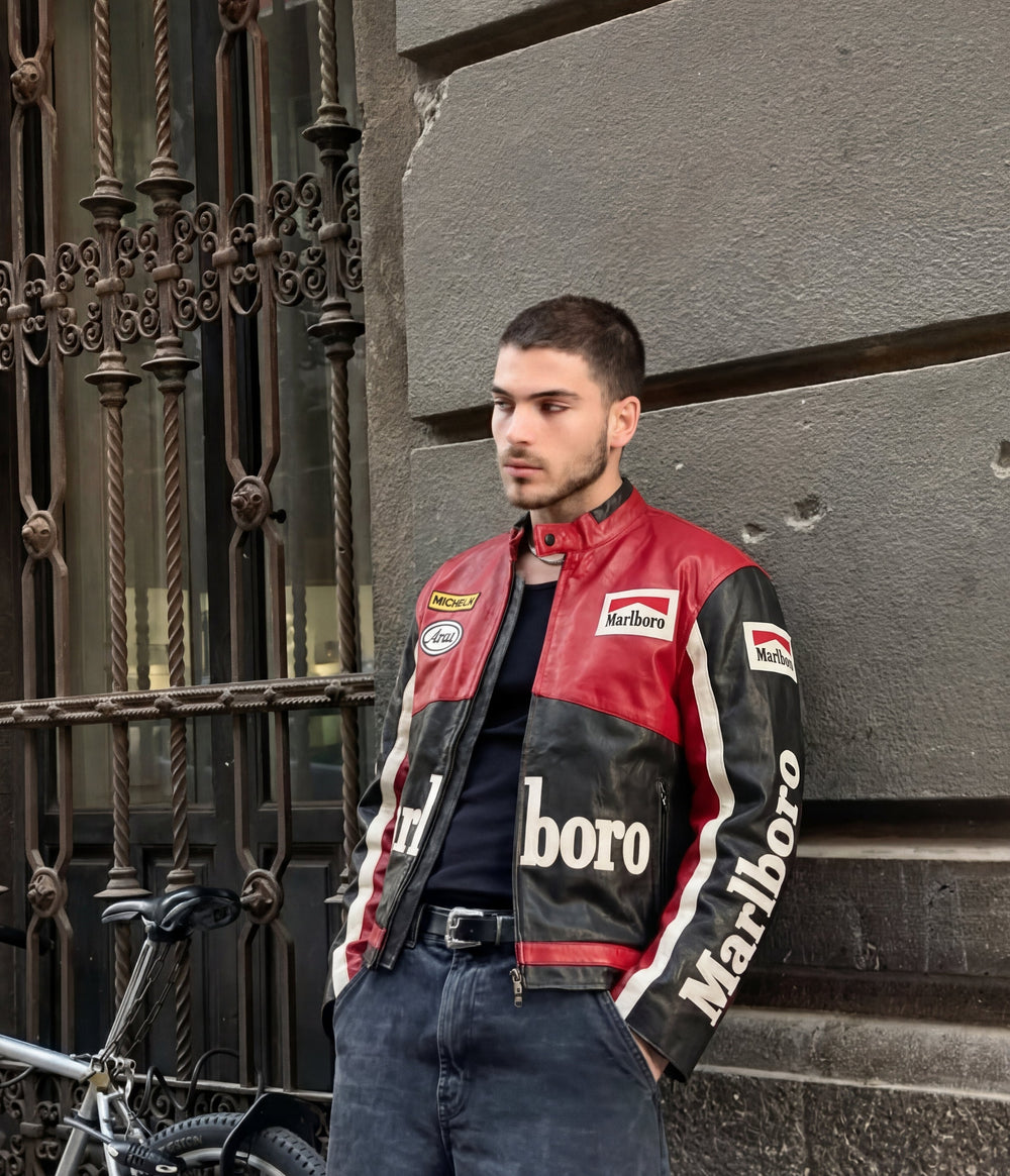 Man in a red, black and white Marlboro vintage leather racing jacket against a stone wall