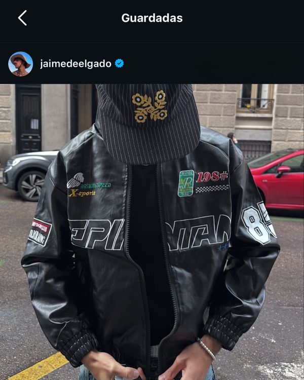 Man in a black leather vintage racing jacket with embroidered patches and a cap