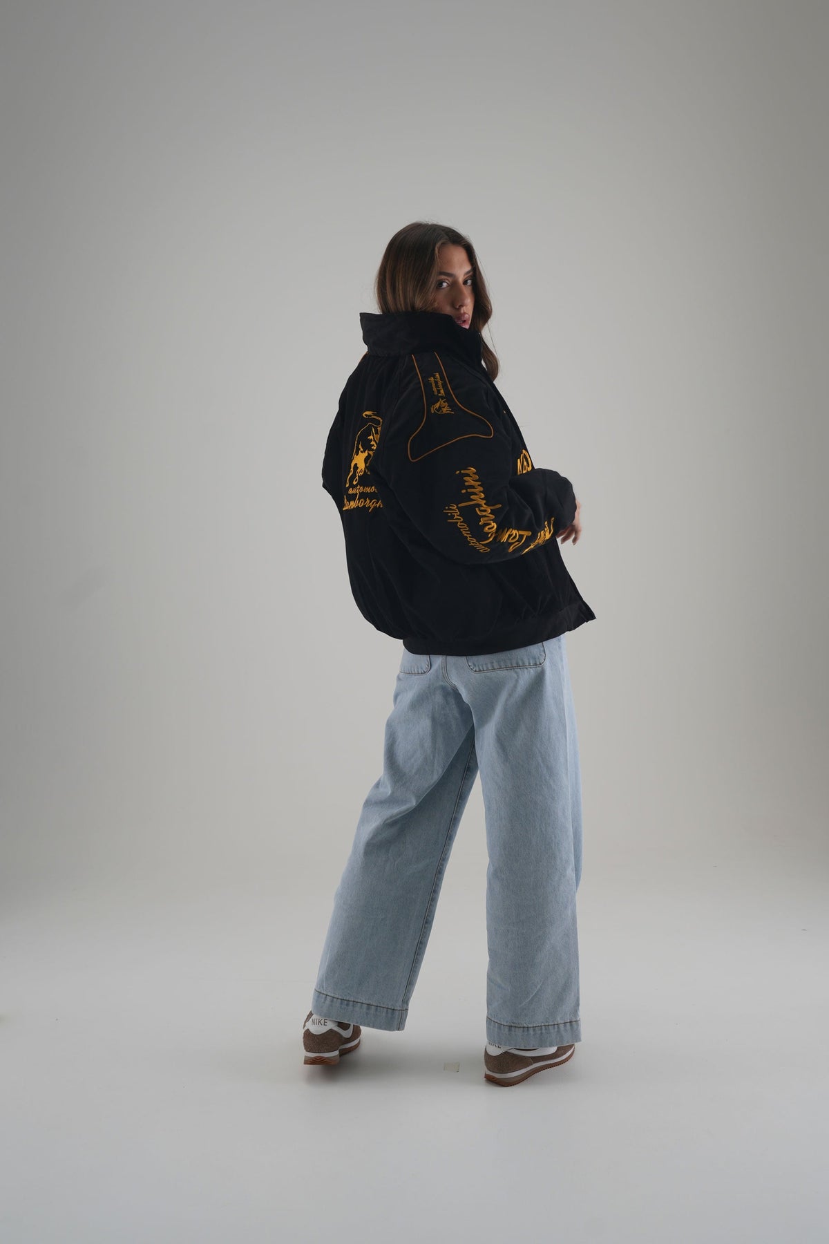 Back view of a woman in a black vintage racing jacket with gold embroidery in the studio