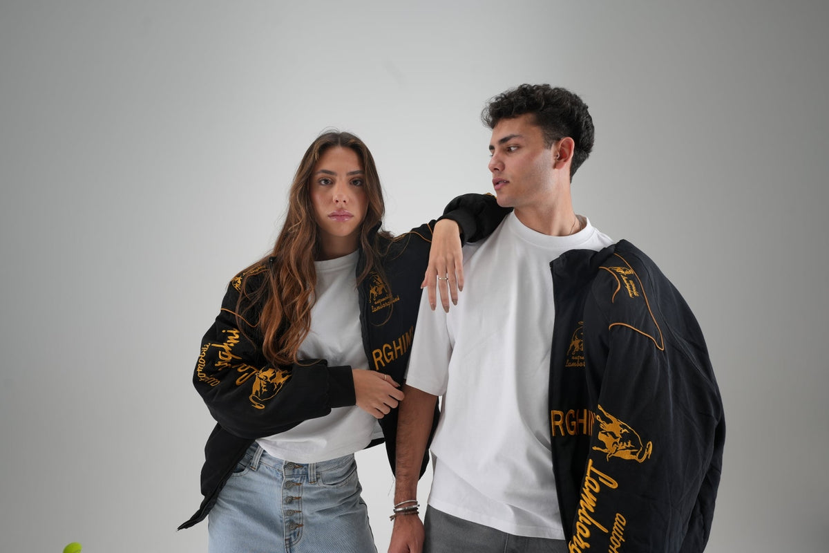 Man and woman wearing black and gold Lamborghini vintage racing jackets in the studio