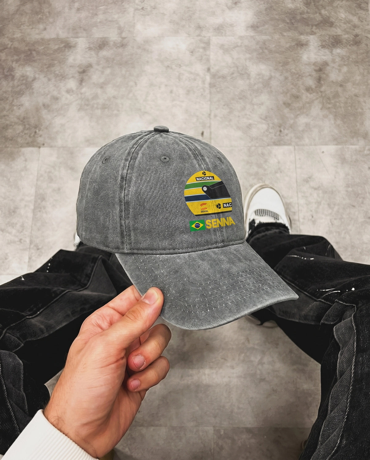 Hand holding the gray Ayrton Senna F1 cap