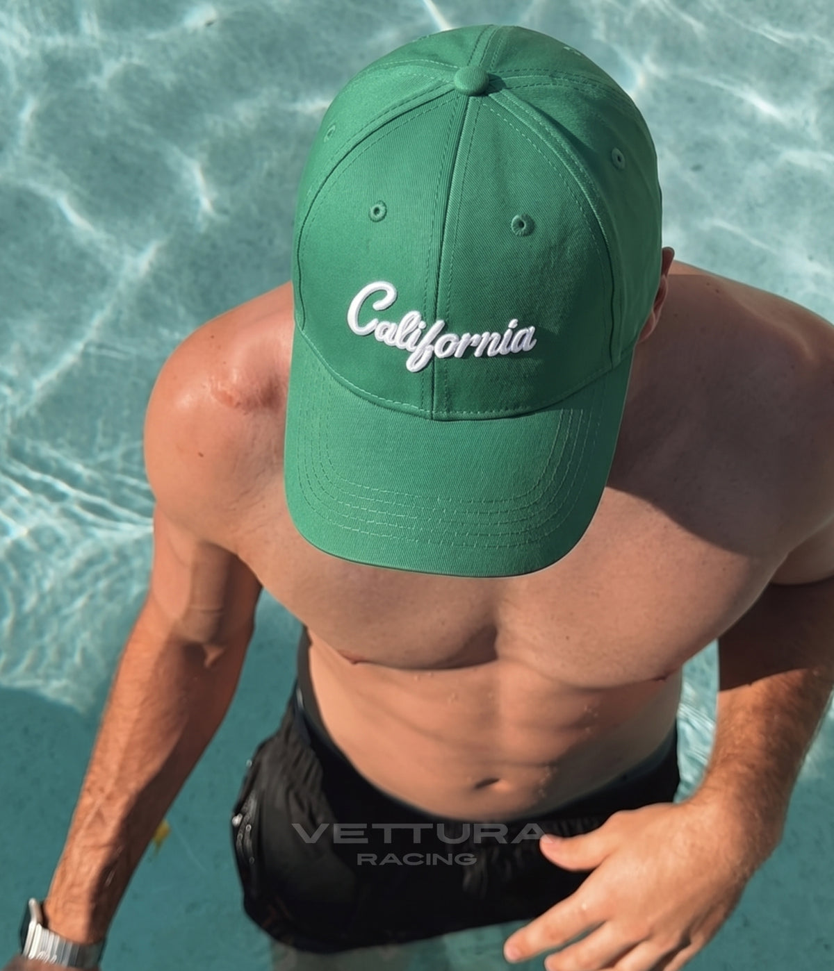 Man wearing the green California cap with white script beside a swimming pool