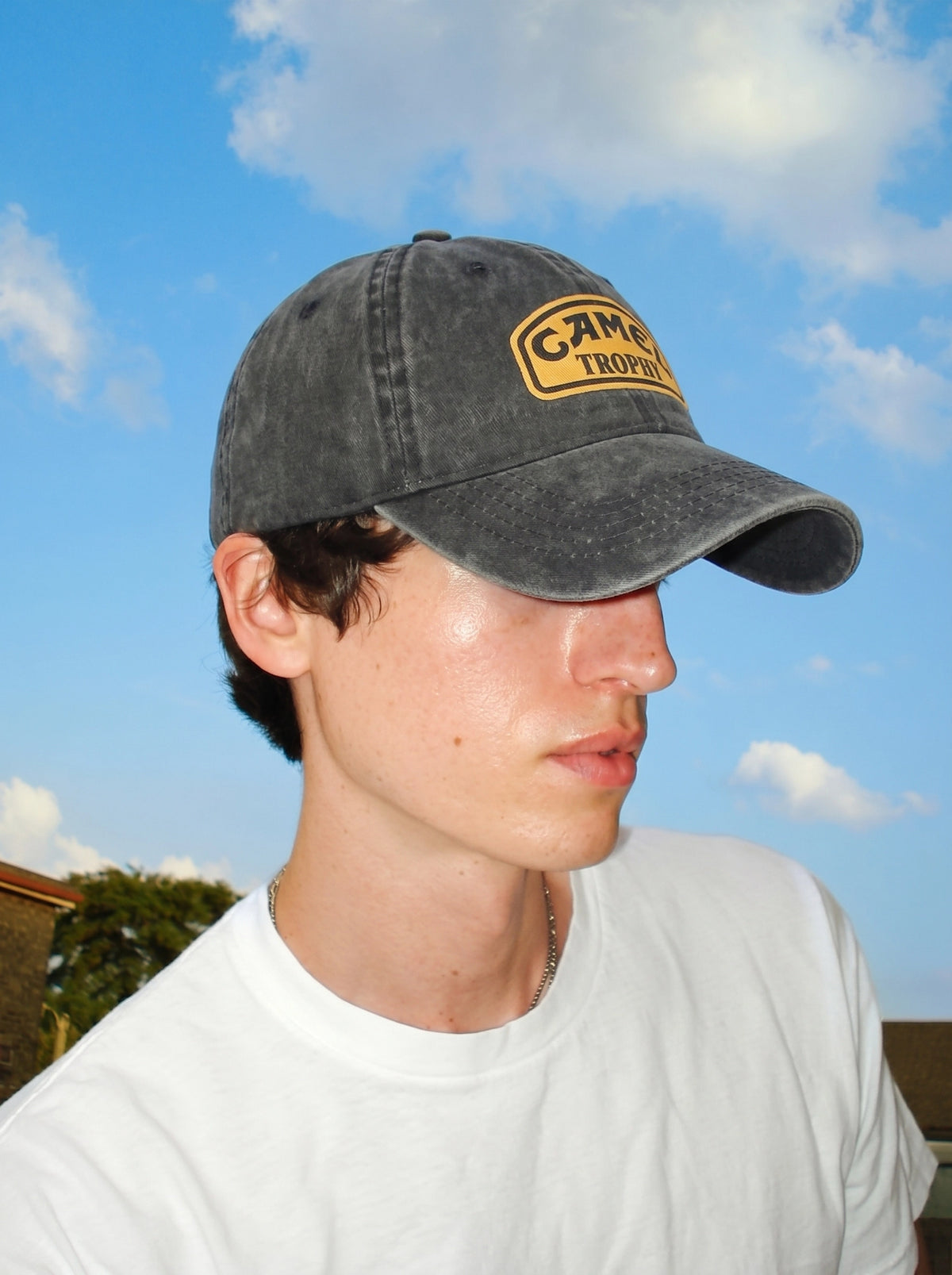 Model wearing the navy Camel Trophy cap against a blue sky