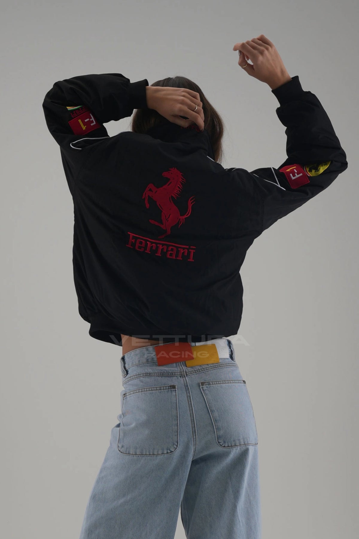 Black Ferrari F1 racing jacket worn open over a plain tee, full length studio shot