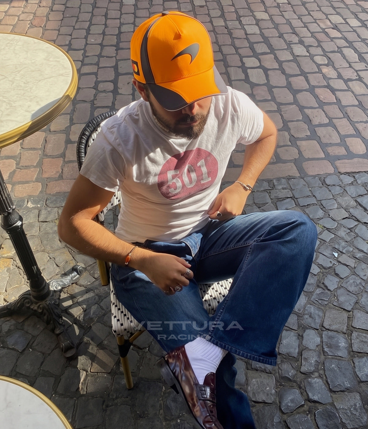 Man wearing the papaya McLaren F1 Team 2025 cap seated at a cafe table