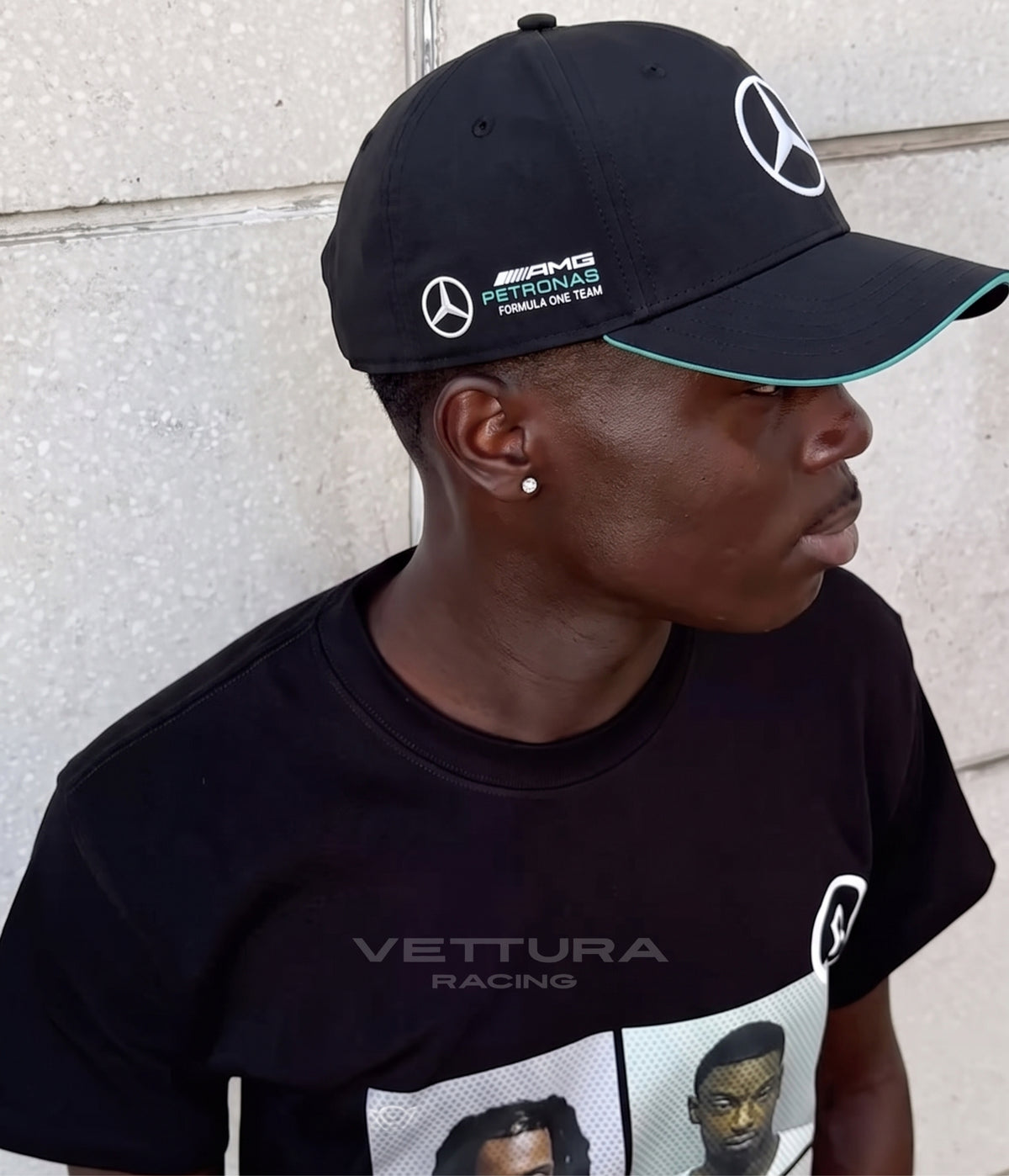 Man in profile wearing the black Mercedes AMG F1 Team cap against a pale wall