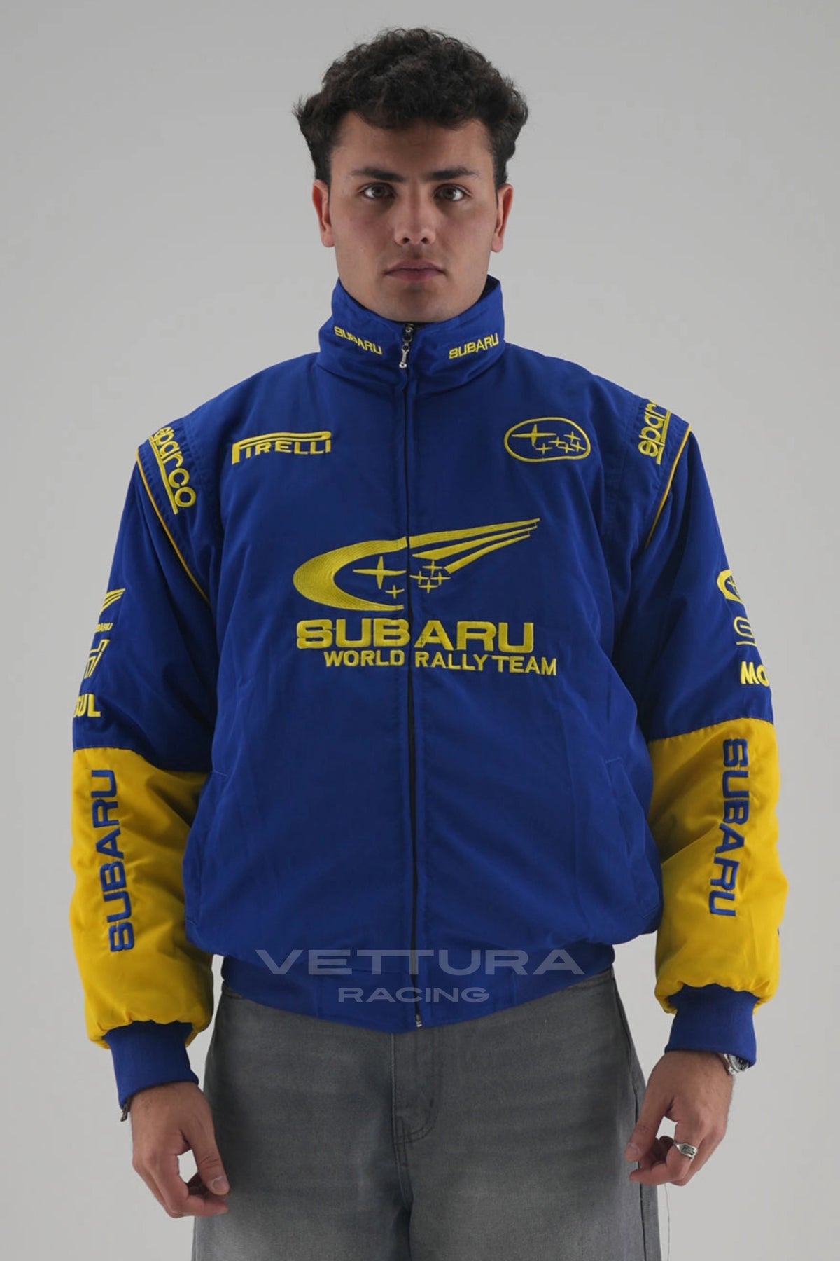 Model wearing the blue and yellow Subaru World Rally vintage racing jacket, front view