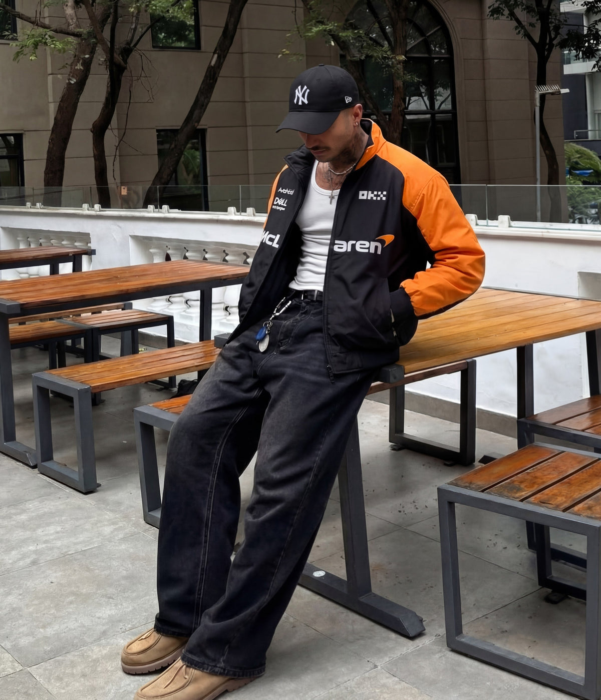 Man in a black and papaya orange McLaren vintage racing jacket leaning on an outdoor table
